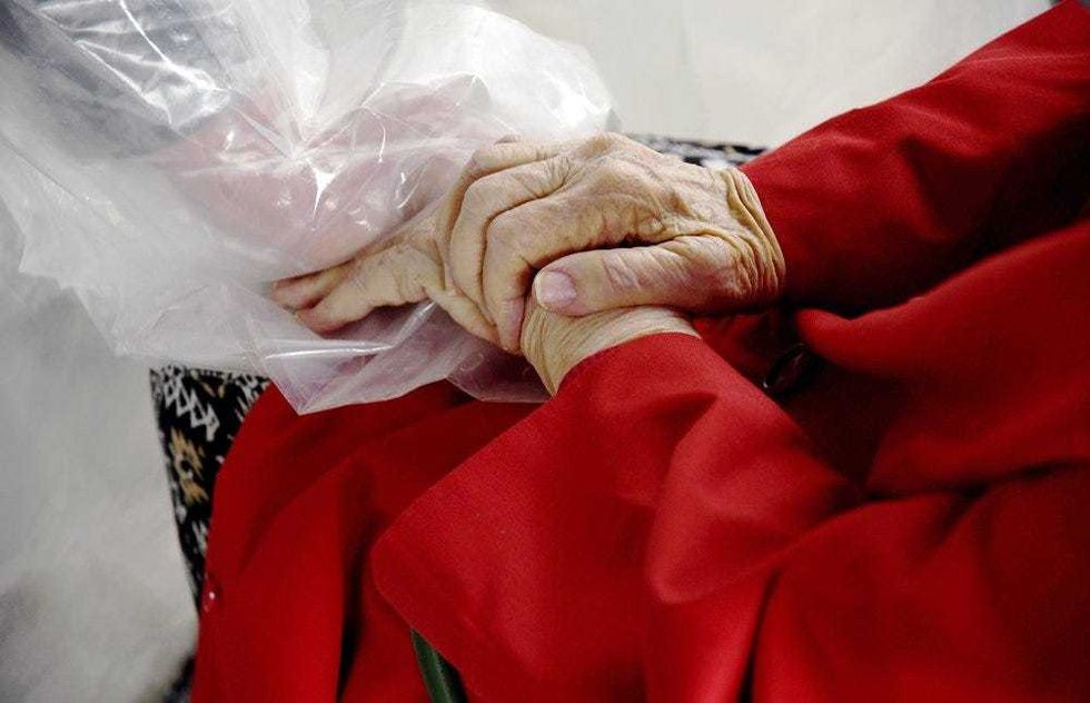 Gregg MacDonald holds hands with his 84-year-old mother, Chloe MacDonald, at a "hug tent" set up outside the Juniper Village assisted living center in Louisville, Colo., on Wednesday, Feb. 3, 2021. The tent includes a construction-grade plastic barrier with built-in plastic sleeves to prevent the spread of the coronavirus.