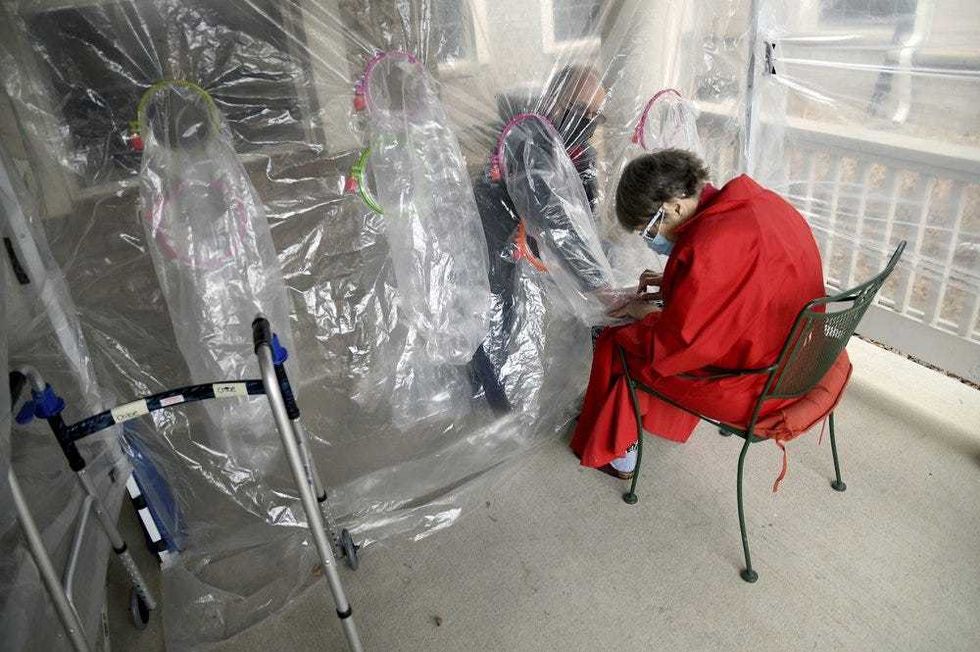 Gregg MacDonald holds hands with his 84-year-old mother, Chloe MacDonald, at a "hug tent" set up outside the Juniper Village assisted living center in Louisville, Colo., on Wednesday, Feb. 3, 2021. The tent includes a construction-grade plastic barrier with built-in plastic sleeves to prevent the spread of the coronavirus.