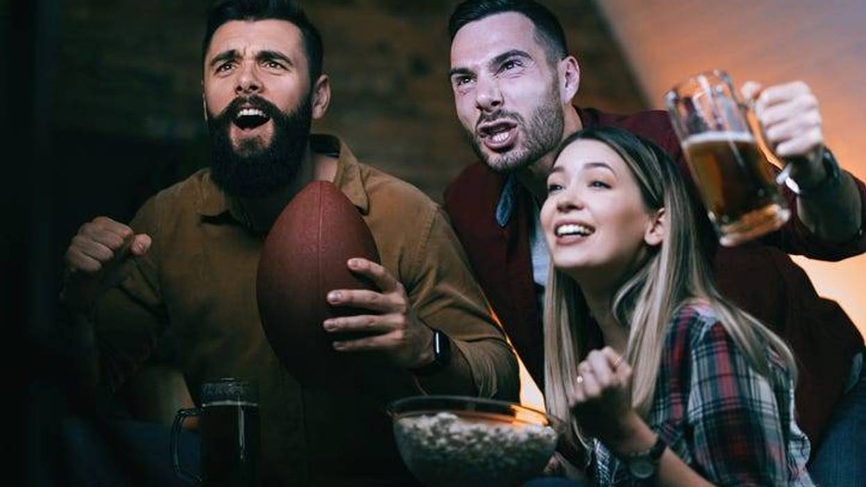 Group of excited friends cheering for their team while watching sport championship on TV at home.