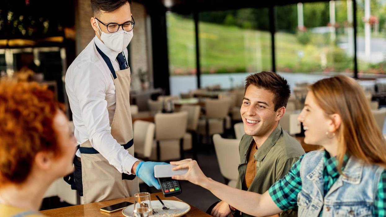 Group of friends paying contactless with mobile phone to a waiter in a cafe. Focus is on waiter.