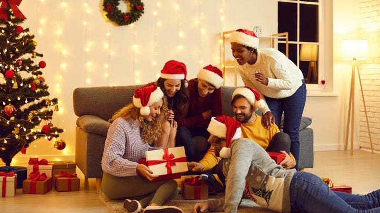 Group of young friends are interested and surprised at opening of magical Christmas present. Amazed and happy people look with curiosity at gift box that their friend. Christmas gifts concept.