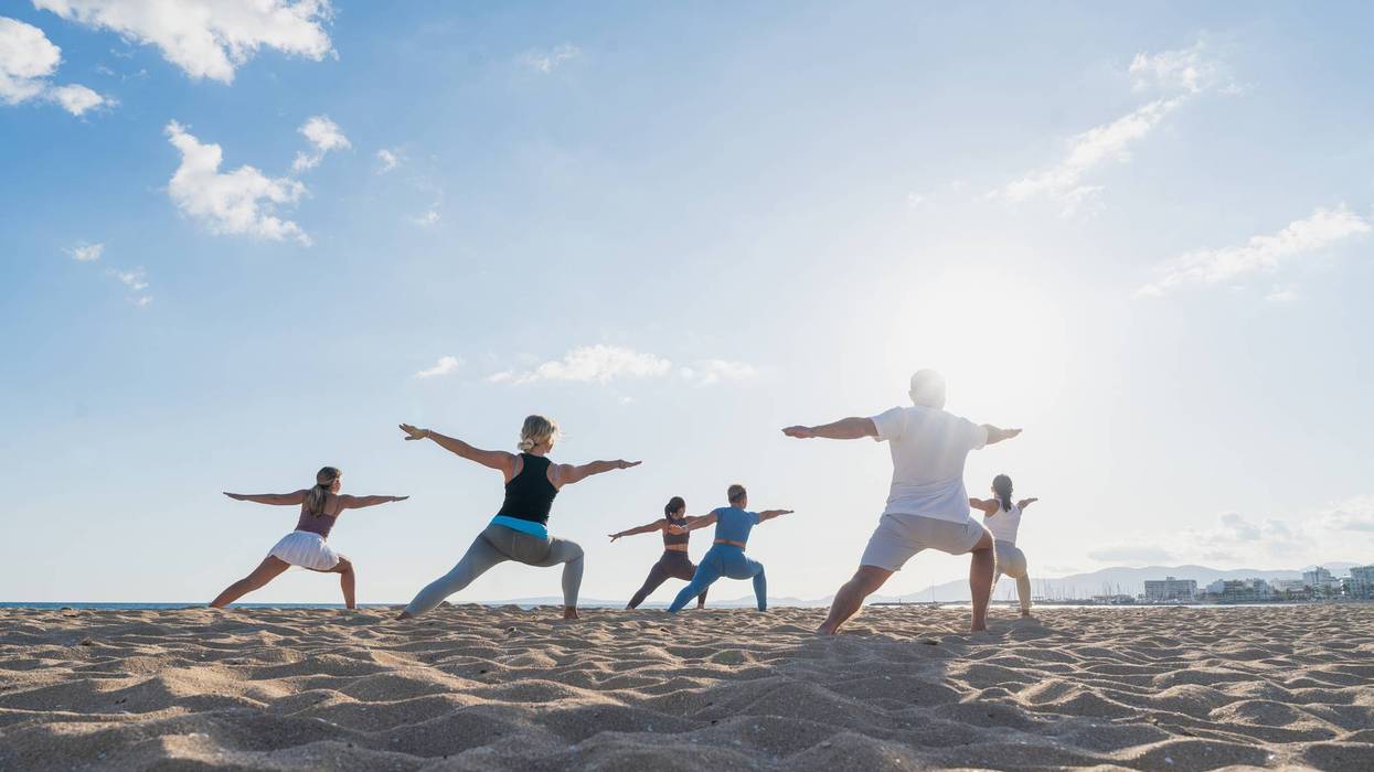 Group practicing warrior pose on beach at sunrise