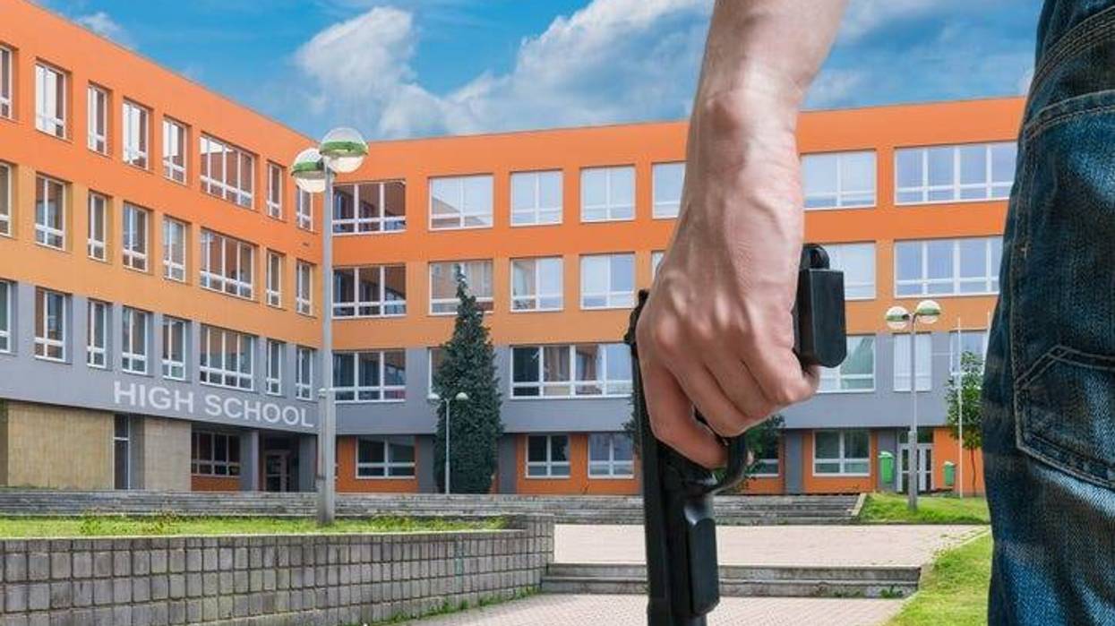 Gun control concept. Young armed man holds pistol in hand in public place near high school.