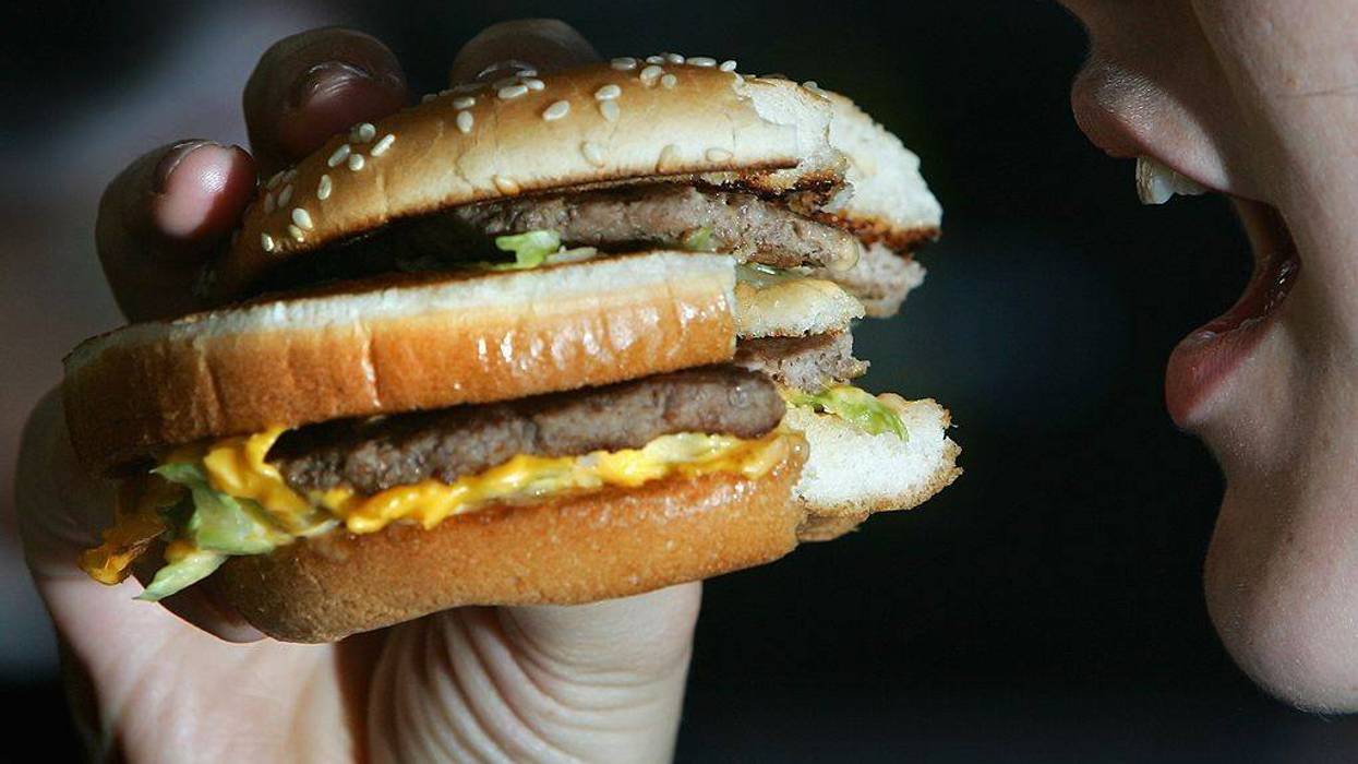 Hand holding a double-patty cheeseburger to an open mouth.