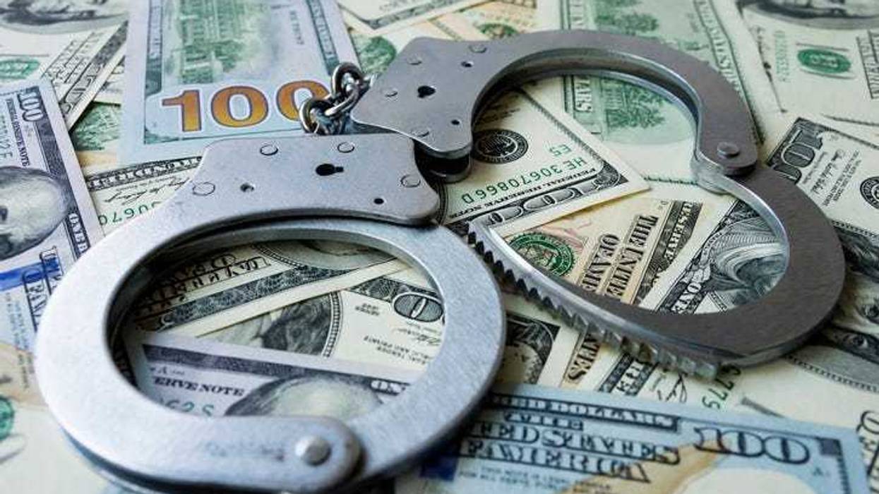 Handcuffs on a pile of US dollar banknotes- symbolic image of a bribe, laundering of money or corruption.