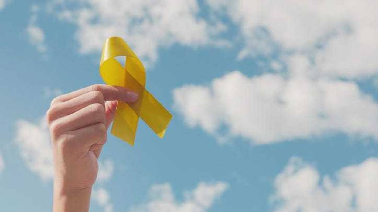 Hands holding yellow gold ribbon over blue sky