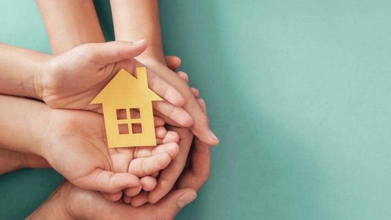 Hands holding yellow paper house on blue background,