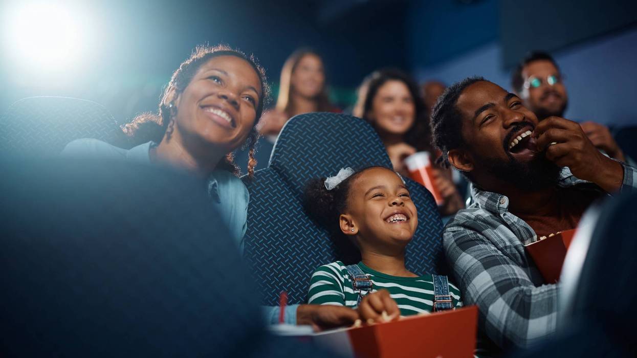 Happy black family laughing while watching funny movie at the cinema.