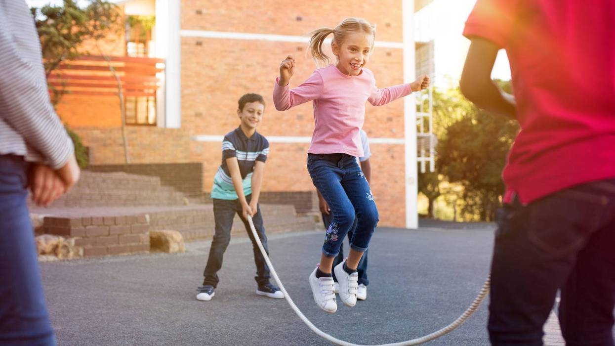 Happy elementary kids playing together with jumping rope outdoor. Children playing skipping rope jumping game and laughing outdoors. .