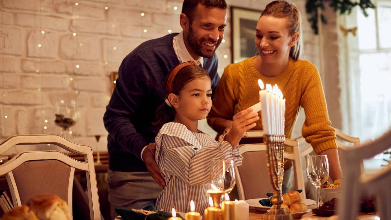 Happy Jewish family lightning the menorah before a meal at dining table