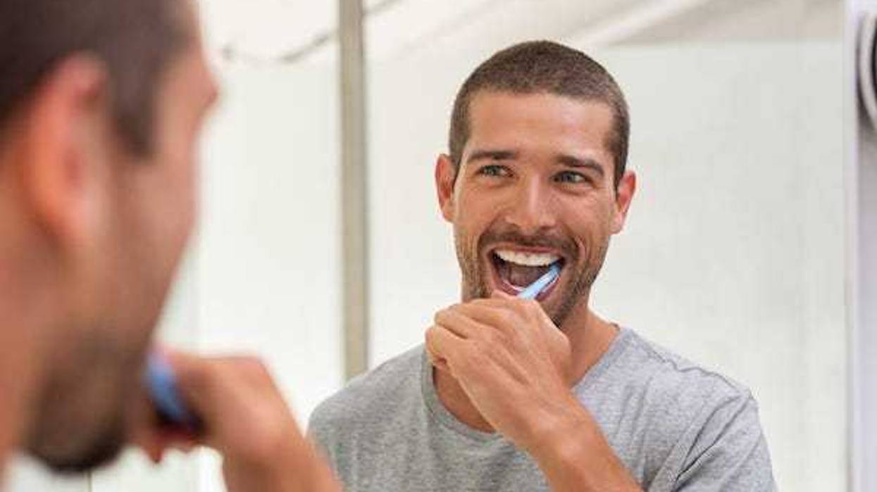 Happy man brushing teeth in the mirror