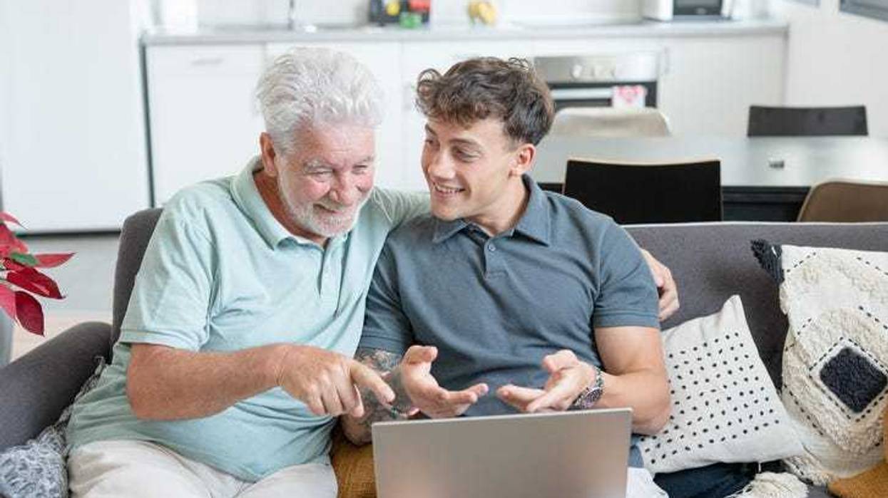 Happy multigenerational family sitting on sofa using laptop together - grandfather with young grandson enjoying carefree moments together learning use of computer