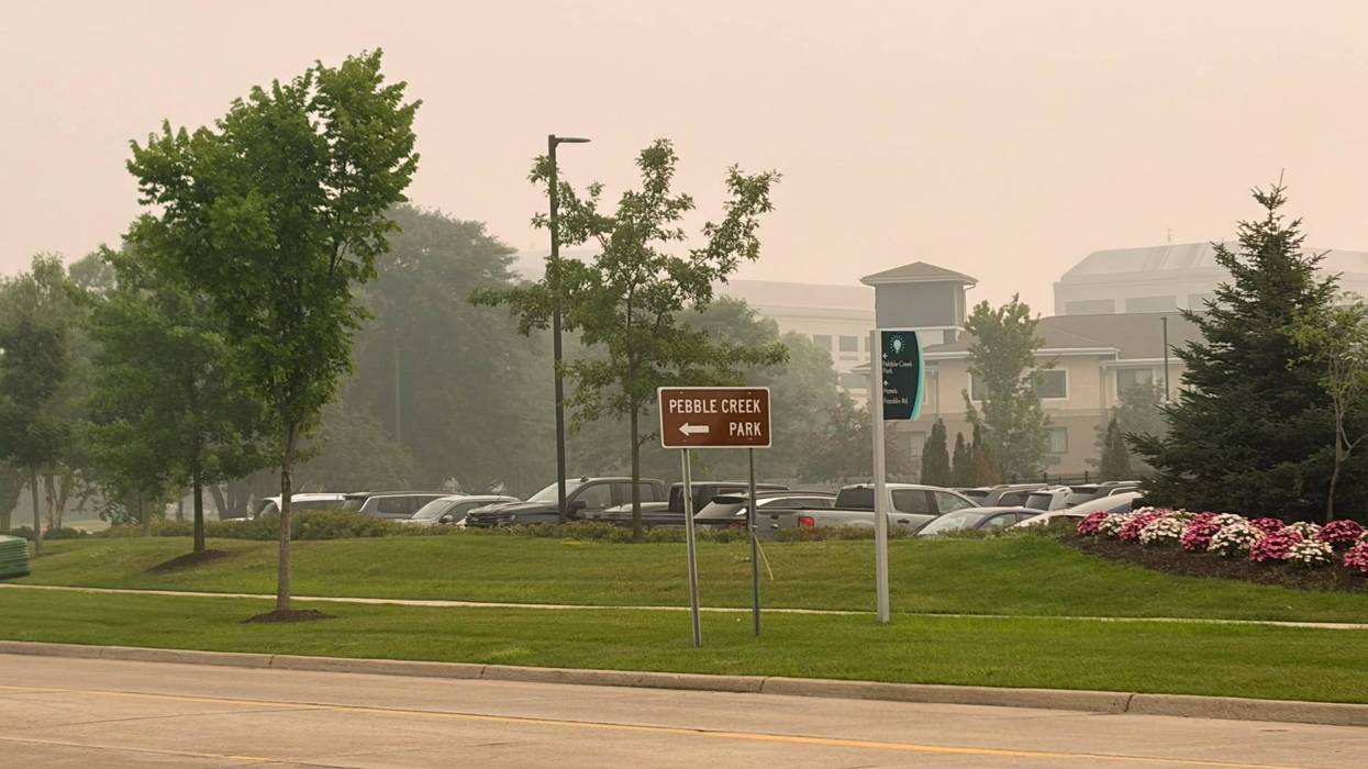 Hazy, orange-tinged sky over a park entrance with a "Pebble Creek Park" sign.