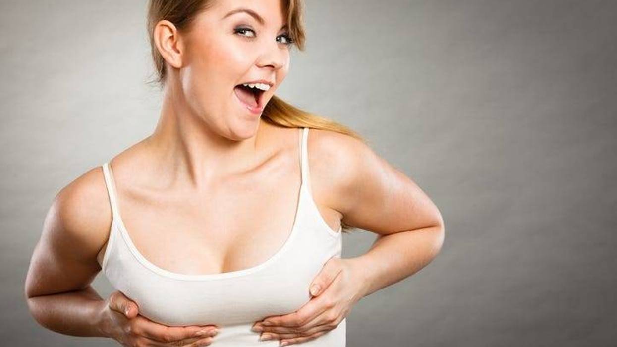 Health care, bosom concept. Young happy joyful woman wearing tshirt holding hands on breast and pushing them up