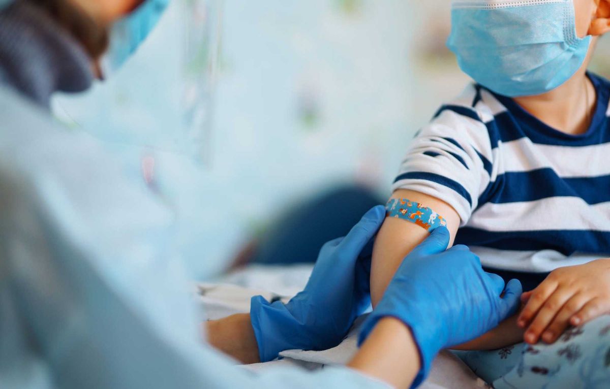 Health care professional putting a bandage on a child after they receive a vaccine shot.
