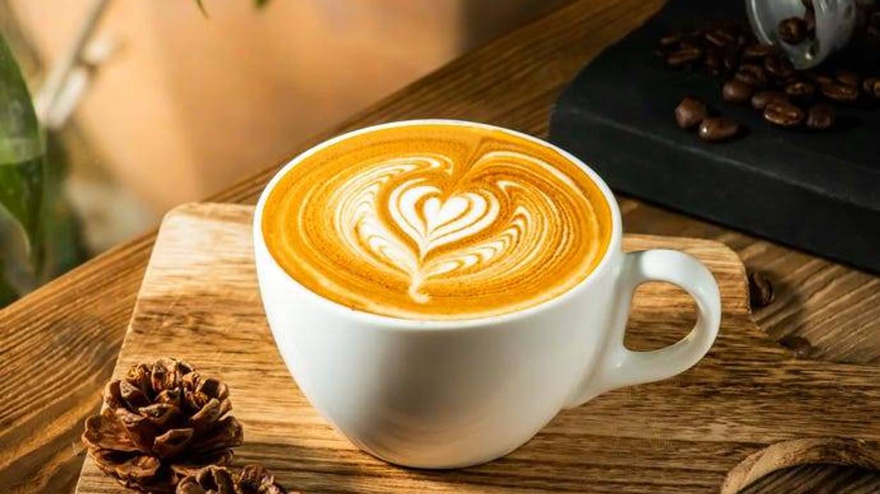 Heart Shaped Latte Art in a White cup with coffee beans isolated on wooden table
