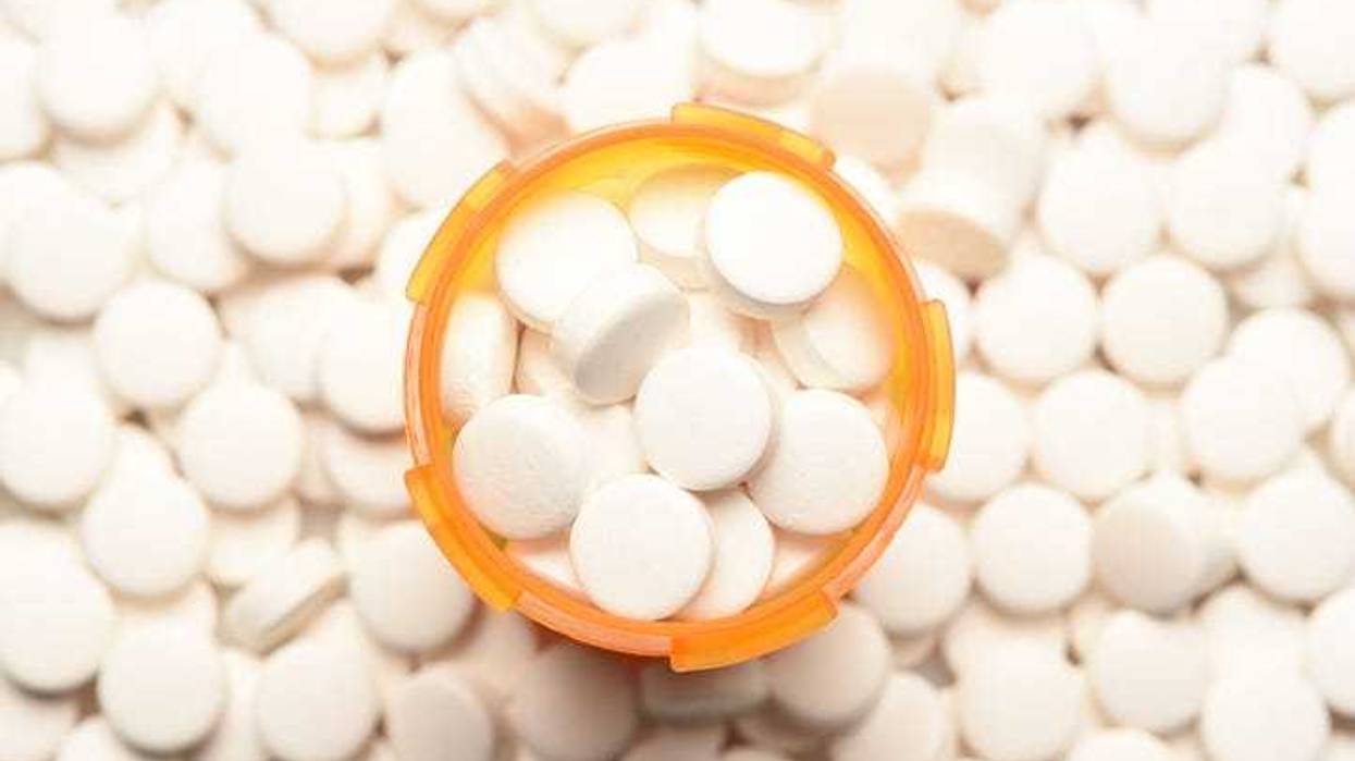 High angle view of a prescription bottled filled with pills surrounded by more of the same tablets.