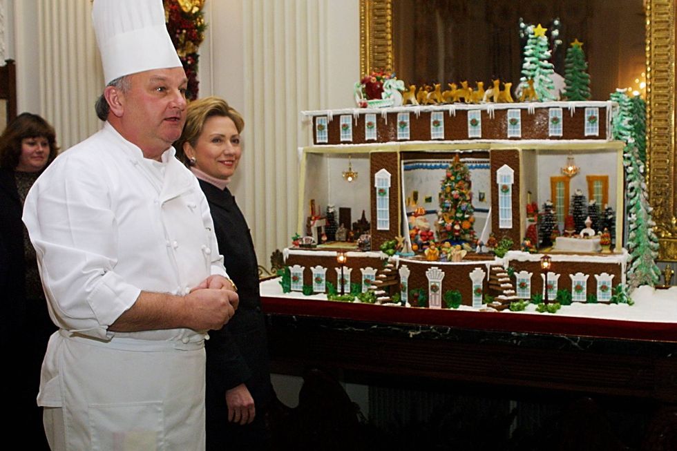 Hillary Rodham Clinton listens to Chef Roland Mesnier explain how a gingerbread house was made December 4, 2000 in the State Dining Room of the White House in Washington, D.C.