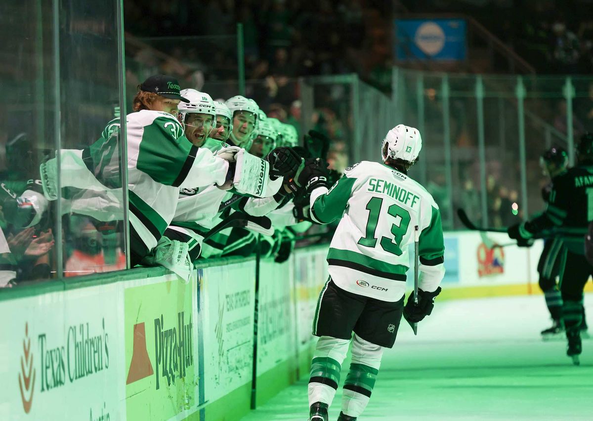 Hockey player Seminoff #13 high-fives excited green-and-white teammates over the bench.