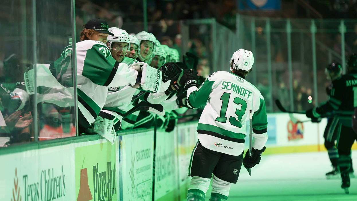Hockey player Seminoff #13 high-fives excited teammates on the bench, wearing green and white.