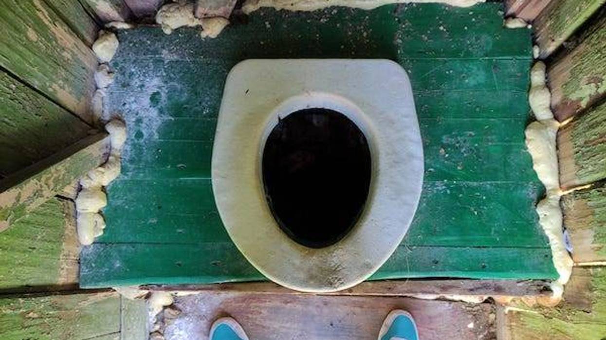 Hole of an old dirty country toilet and foots in sneakers