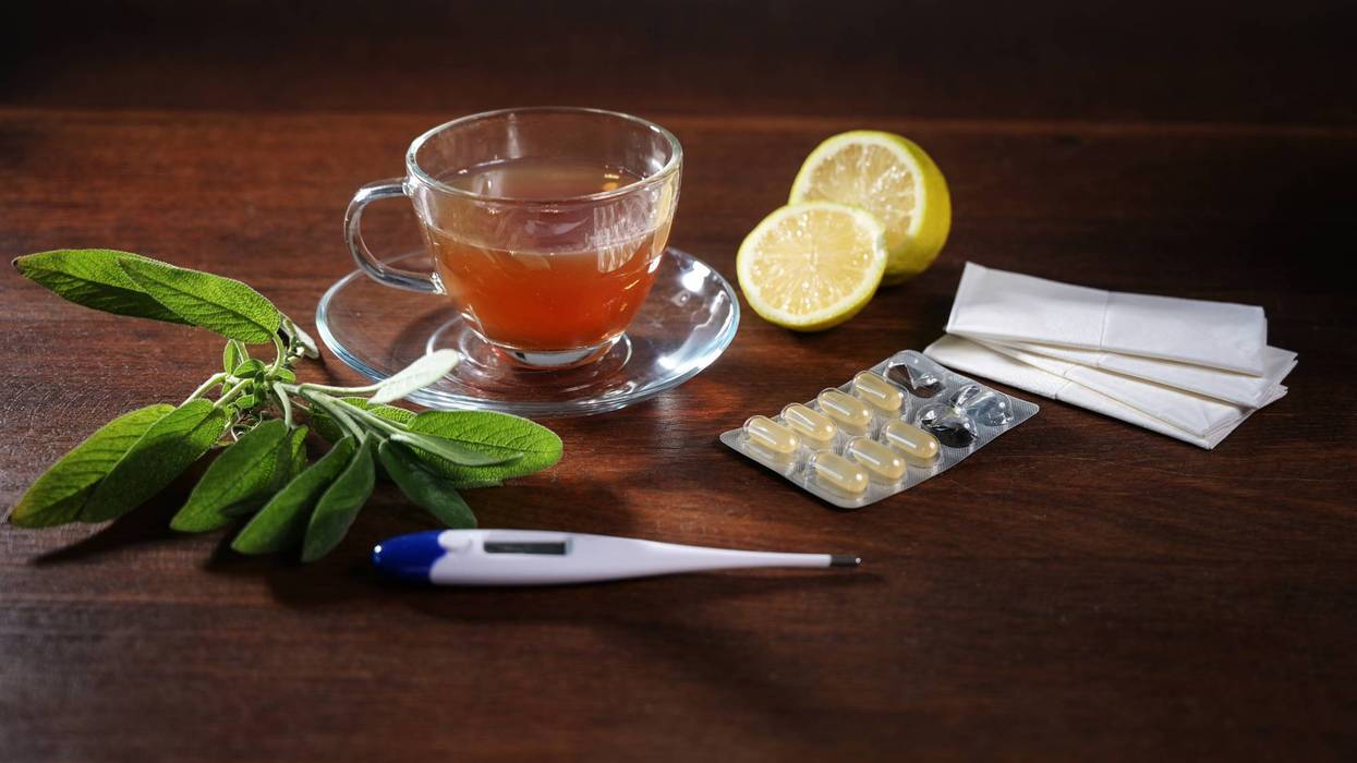 Home remedy treatments against cold and flu, such as sage tea, lemon, pills, tissues and a fever thermometer on a dark wooden table, health concept, copy space, selected focus