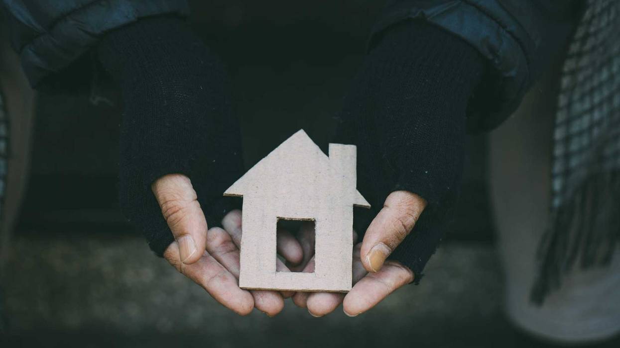 Homeless person holding a cut out of a home.