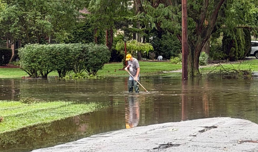 Homewood resident Tony Ferracane uses a rake to clear storm drains on a flooded street in his neighborhood.