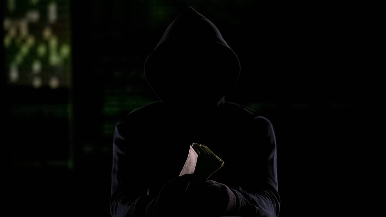 Hooded man in darkness holding cash, murder-for-hire reward or stolen money