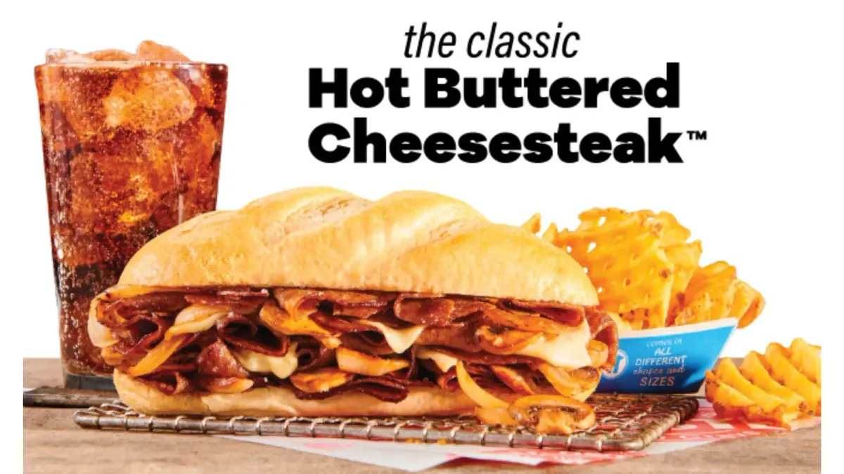 Hot Buttered Cheesesteak sub, waffle fries, and soda. Text: the classic Hot Buttered Cheesesteak™.