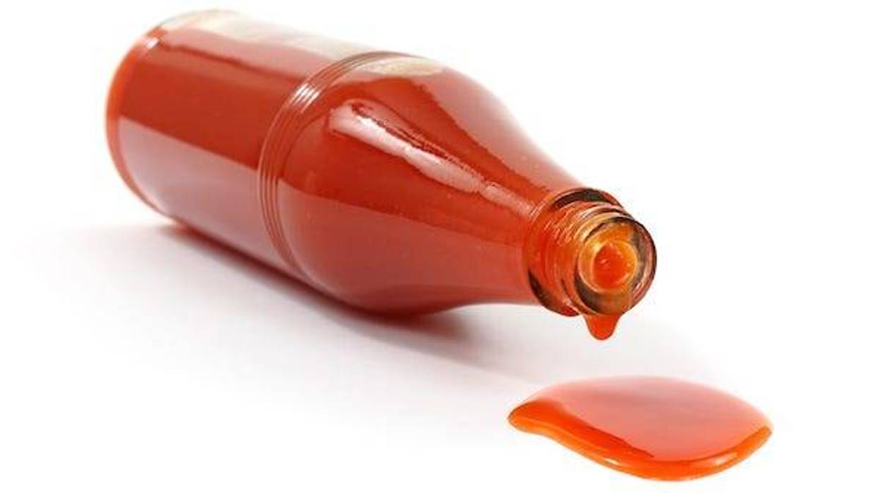 Hot sauce spilling from bottle against white background