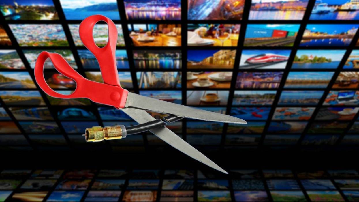 Image shows scissors cutting through a coaxial cable in front of a bank of tv screens