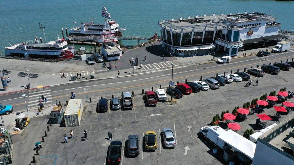 In an aerial view, cars and tables fill a parking lot next to a restaurant and bay cruise terminal at San Francisco's Fisherman's Wharf tourist destination on June 14, 2021 in San Francisco, California.