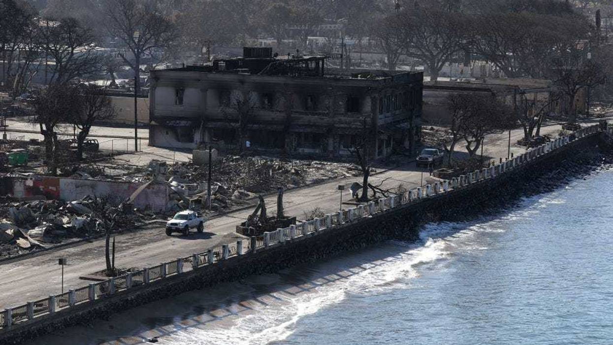 In an aerial view, cars drive businesses that were destroyed by a wildfire on August 11, 2023 in Lahaina, Hawaii. Dozens of people were killed and thousands were displaced after a wind-driven wildfire devastated the town of Lahaina on Tuesday. Crews are continuing to search for missing people. (Photo by Justin Sullivan/Getty Images)