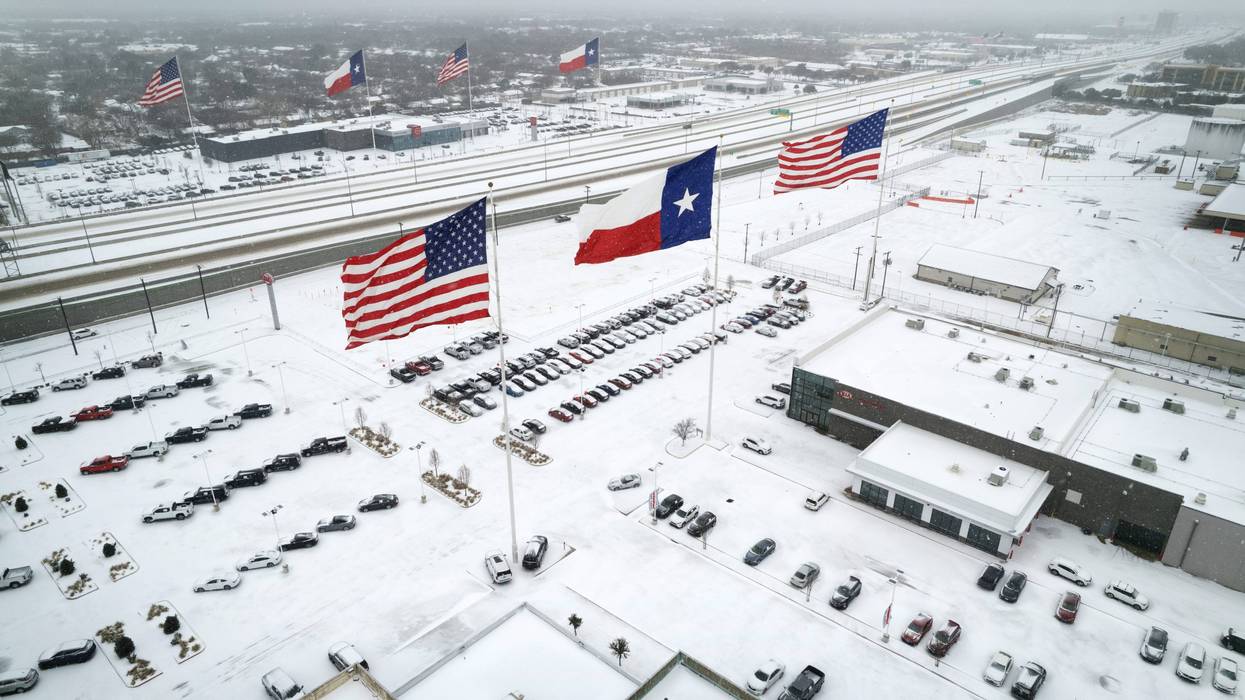 In an aerial view, U.S. and Texas state flags fly over car dealerships as light traffic moves through snow and ice on U.S. Highway 183 on Feb. 3, 2022, in Irving, Texas. A winter storm blanketed much of Texas with snow, sleet, and freezing rain, as it swept east, also affecting much of the midwest and eastern United States.
