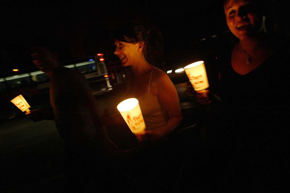 In the dark of a night without power, people in New York walk down the street holding candles.
