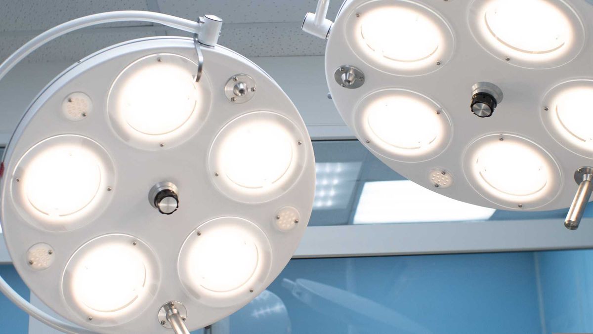 In the hospital, a surgical lamp shines under the ceiling above the surgical table. Two large round operating lamps are lit with many diot lights..
