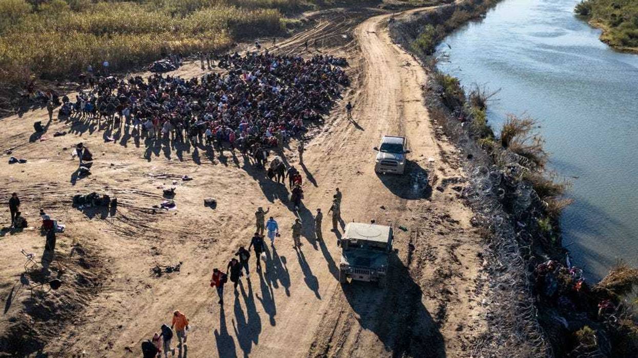 In this aerial view, Texas National Guard troops direct a group of more than 1,000 immigrants towards a U.S. Border Patrol processing center after they crossed the Rio Grande from Mexico on December 18, 2023 in Eagle Pass, Texas.