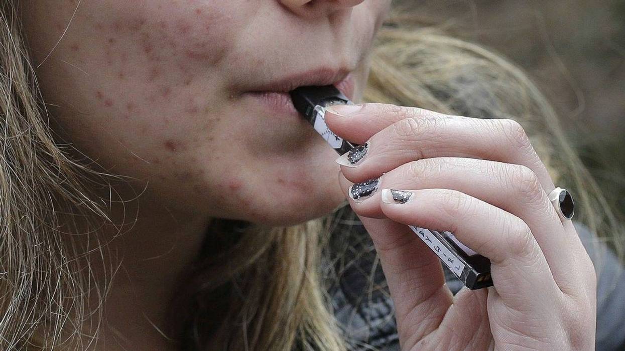 In this April 11, 2018 file photo, a high school student uses a vaping device near a school campus in Cambridge, Mass.