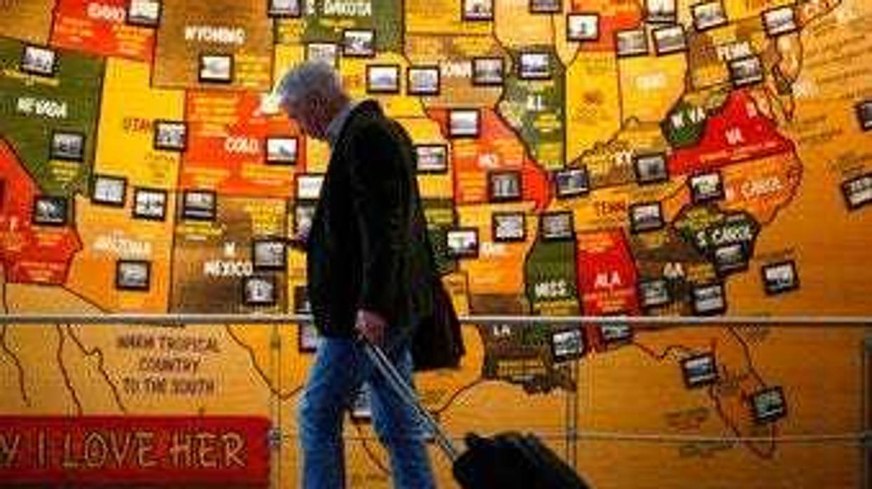 In this March 18, 2020 photo, a traveler checks his mobile telephone while passing a map of the United States on the way to the security checkpoint in the main terminal in Denver International Airport in Denver. (AP Photo/David Zalubowski)