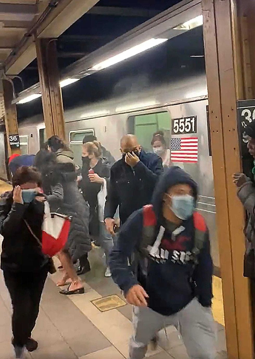 In this photo from social media video, passengers run from a subway car in a station in the Brooklyn borough of New York, Tuesday, April 12, 2022