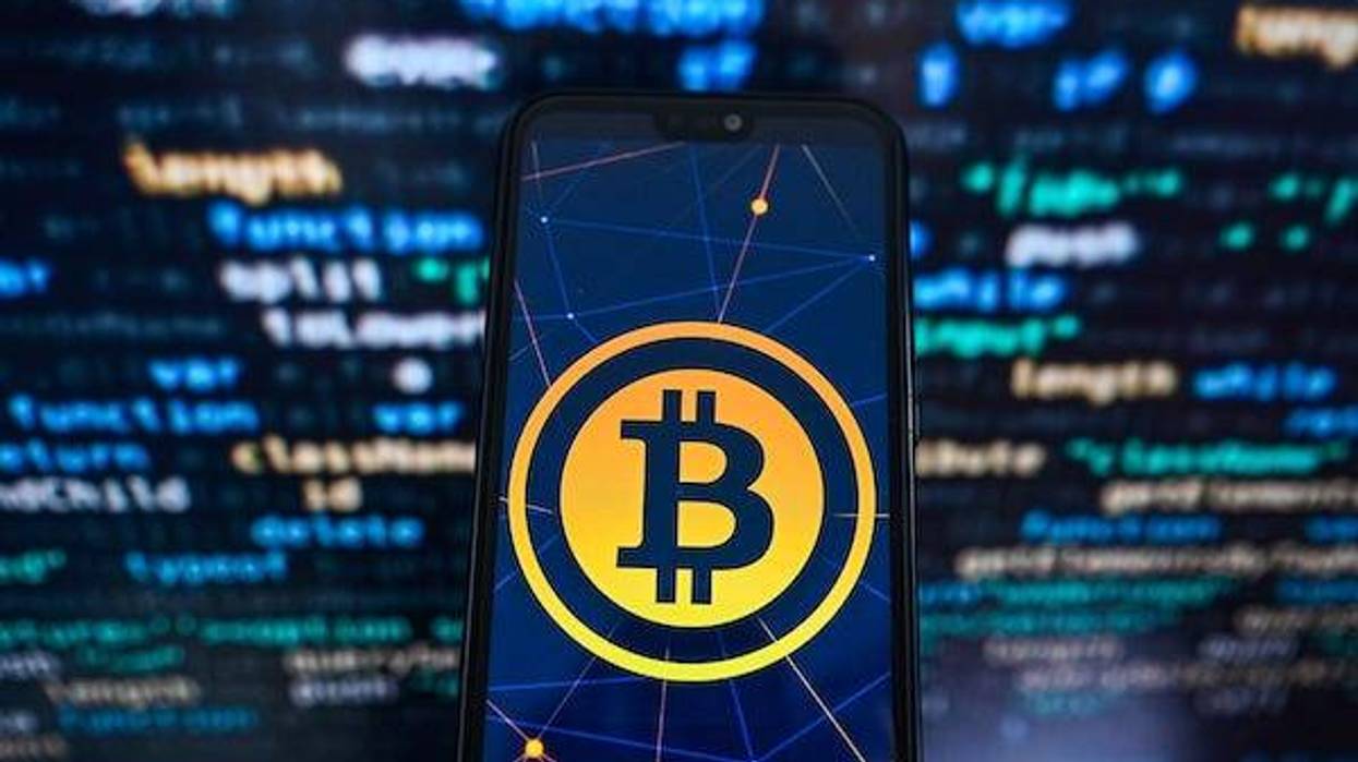 In this photo illustration a Bitcoin logo displayed on a smartphone with programing code on the background