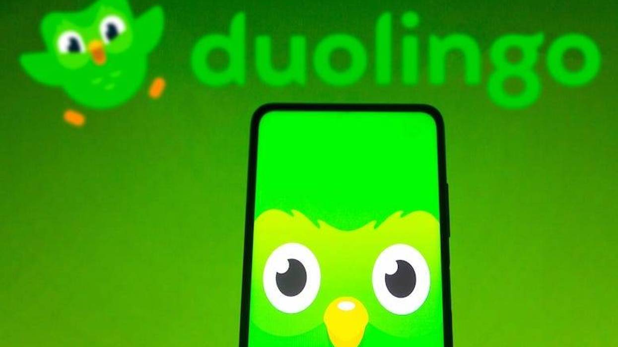 In this photo illustration the Duolingo logo seen displayed on a smartphone and in the background