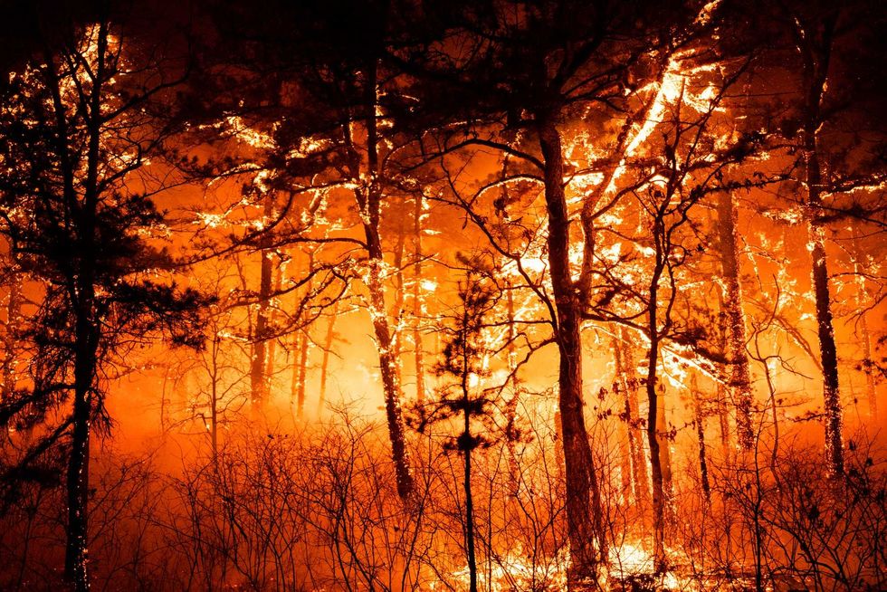 In this photo provided by the New Jersey Department of Environmental Protection, a massive 2,500-acre forest fire burns in Ocean County, N.J., early Wednesday, April 12, 2023, as firefighters battle the blaze
