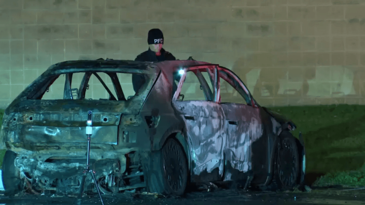 Investigators search the burned out remains of a car in a parking lot near the Philadelphia Airport early Sunday morning.