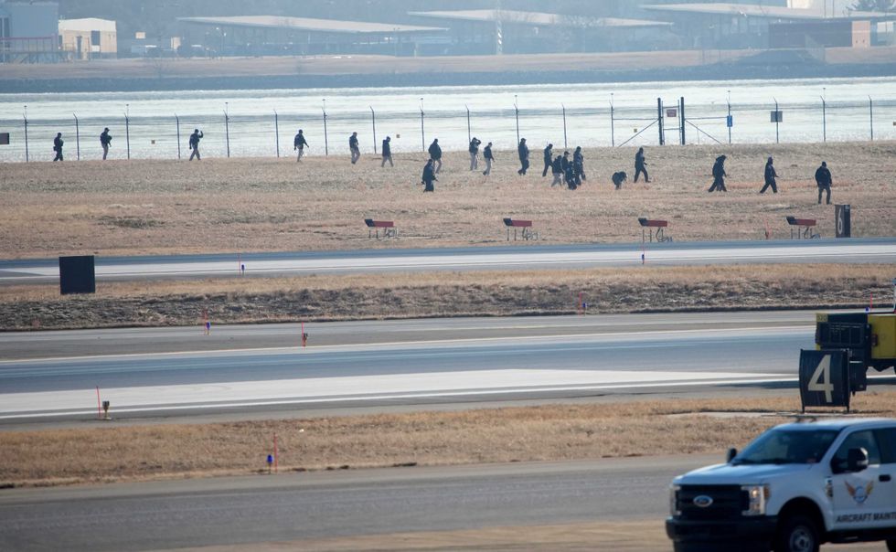 Investigators walk the grounds of the Reagan National Airport as they work near the crash last night of the American Airlines plane on the Potomac River as it approached the Reagan National Airport on January 30, 2025 in Arlington, Virginia