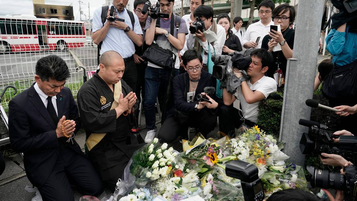 Japanese Diet member, Kenta Izumi, left, and Buddhist monk, Matsumoto Genkun, pay respects at a makeshift memorial site in front of burned Kyoto Animation Studio building, background left, Friday, July 19, 2019, in Kyoto, Japan.