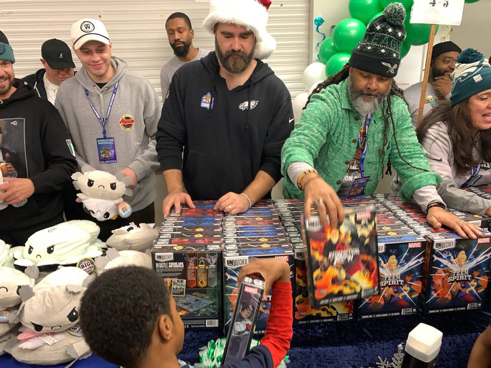 Jason Kelce (center), flanked by comedian Pete Davidson to his right and Board of Education President Reginald Streater to his left, hand out toys at the Alliance for Progress Charter School in North Philadelphia on Tuesday, Dec. 17.