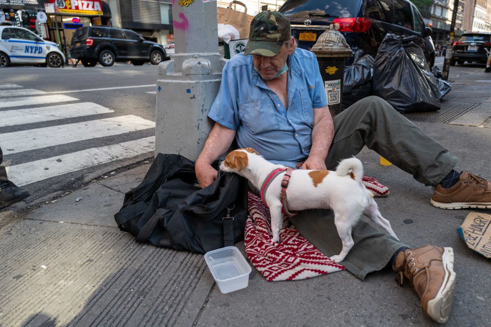 John, who is homeless, sits with his dog Daisy on a Manhattan street during a heat wave on July 22, 2022 in New York City.