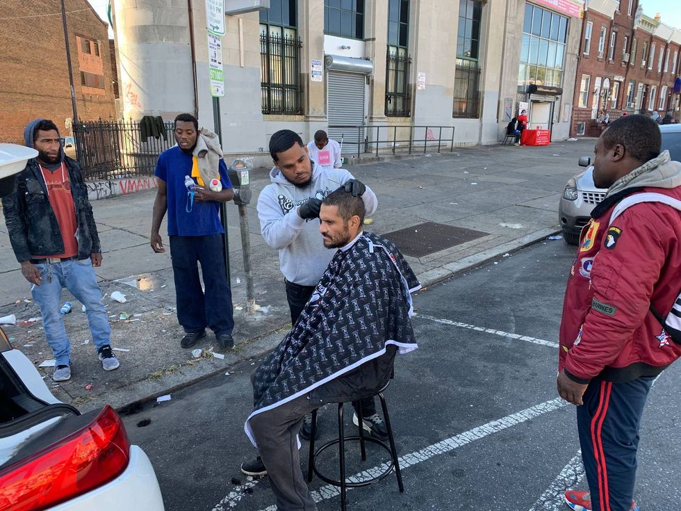 Joshua Santiago gives Angel Ramirez a haircut while other men gather to wait their turn.